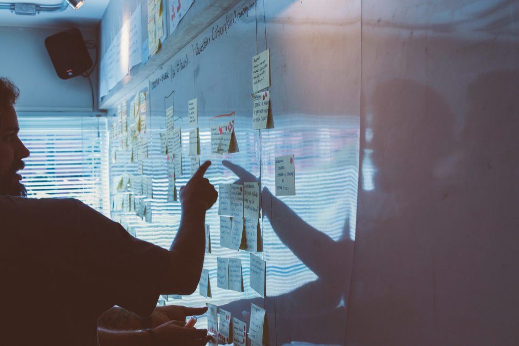 financestream employee pointing to a post-it note on a whiteboard evaluating marketing effots